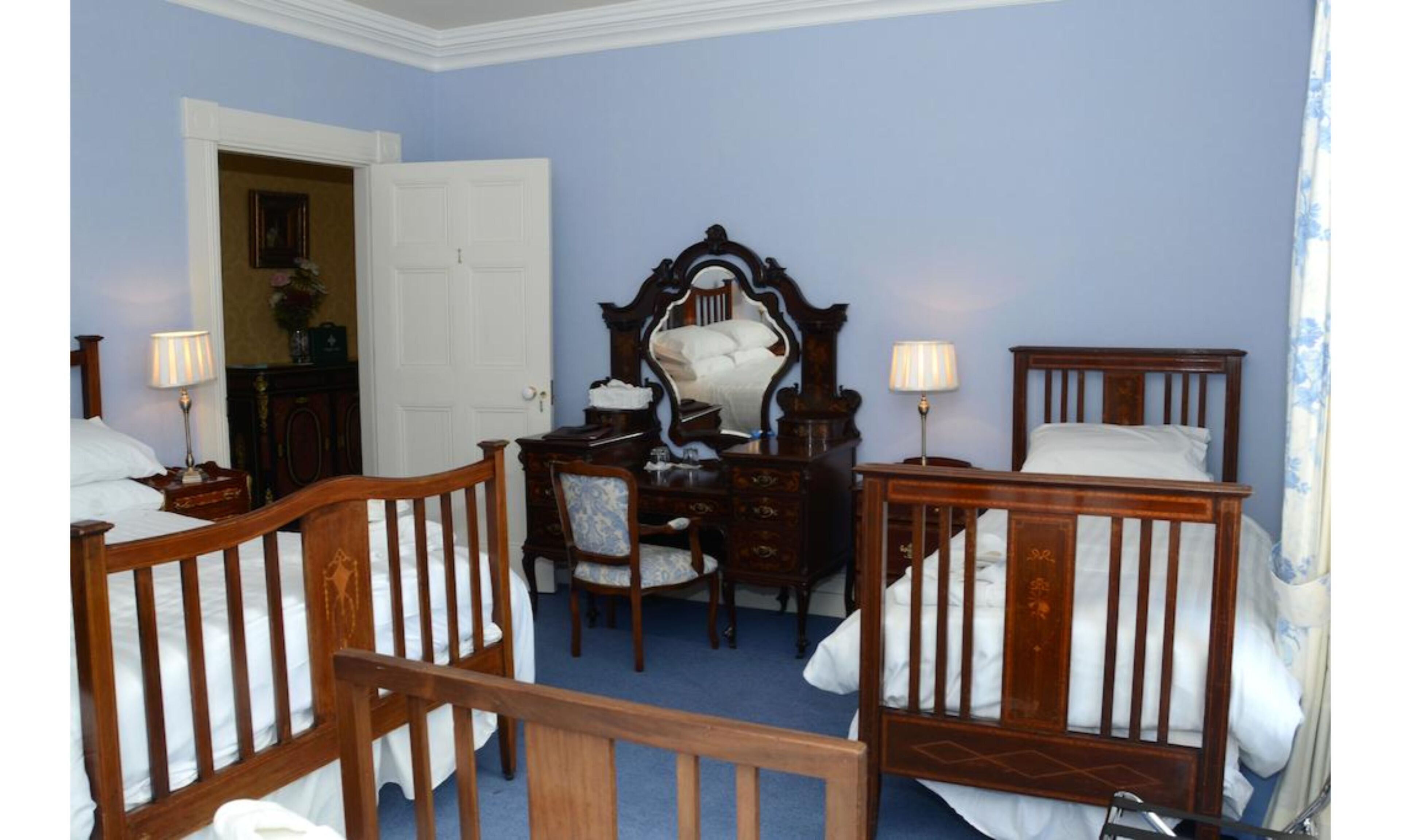 A room with two wooden beds, a wooden dresser, a mirror, and two lamps.
