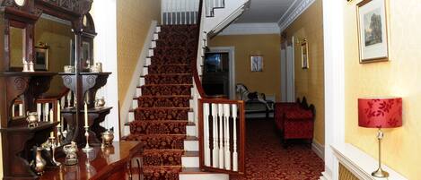 A grand staircase with a red carpet, a wooden console table with various items, and a framed picture on the wall.