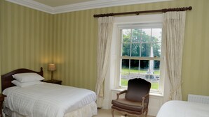 A bedroom with two beds, a nightstand, a chair, and a window with curtains. - Cannaway House B&B (Macroom)