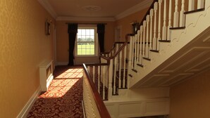 A staircase with white balusters and a red carpeted floor leading to a door with a view of a green field. - Cannaway House B&B (Macroom)