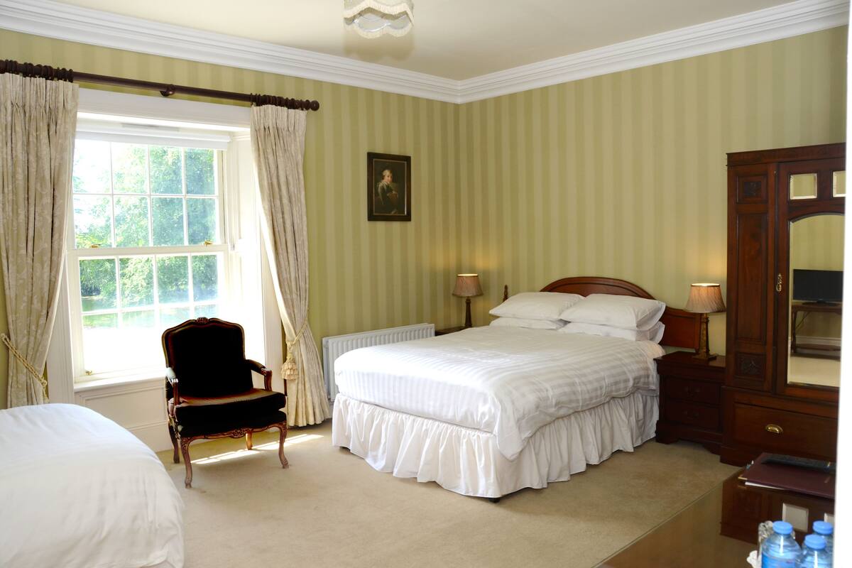 A hotel room with a large bed, a chair, a dresser, and a window with curtains.