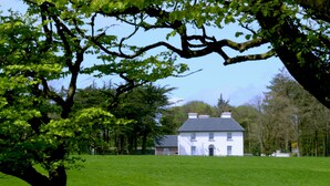 A white house with a grey roof, surrounded by a green field and trees. - Cannaway House B&B (Macroom)
