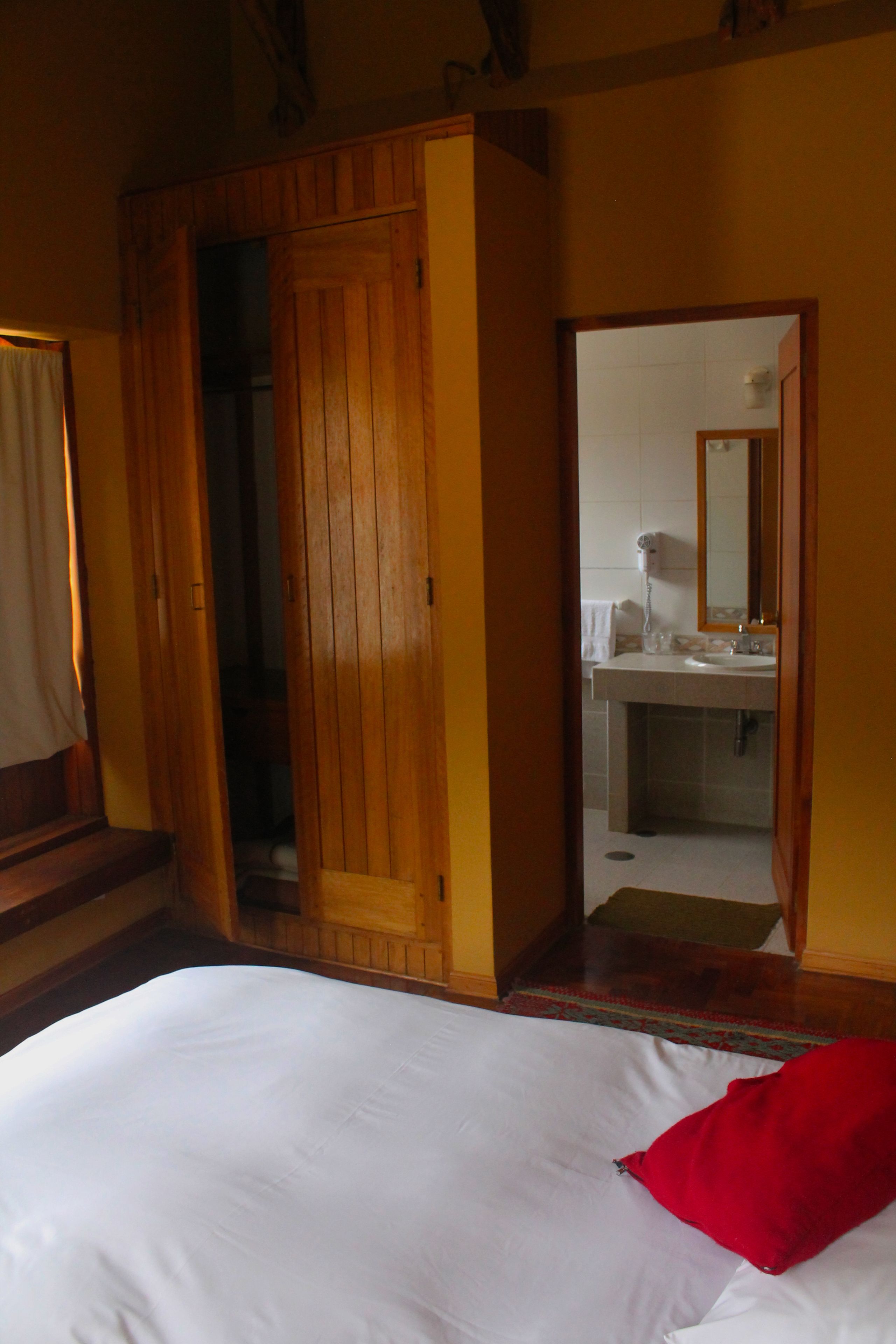 A bedroom with a wooden wardrobe, a bed with white bedding, and a red pillow.