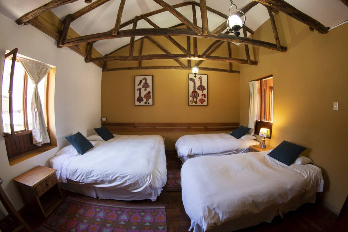 Une chambre avec deux lits, des poutres en bois au plafond, un tapis à motifs et des œuvres d’art accrochées aux murs.