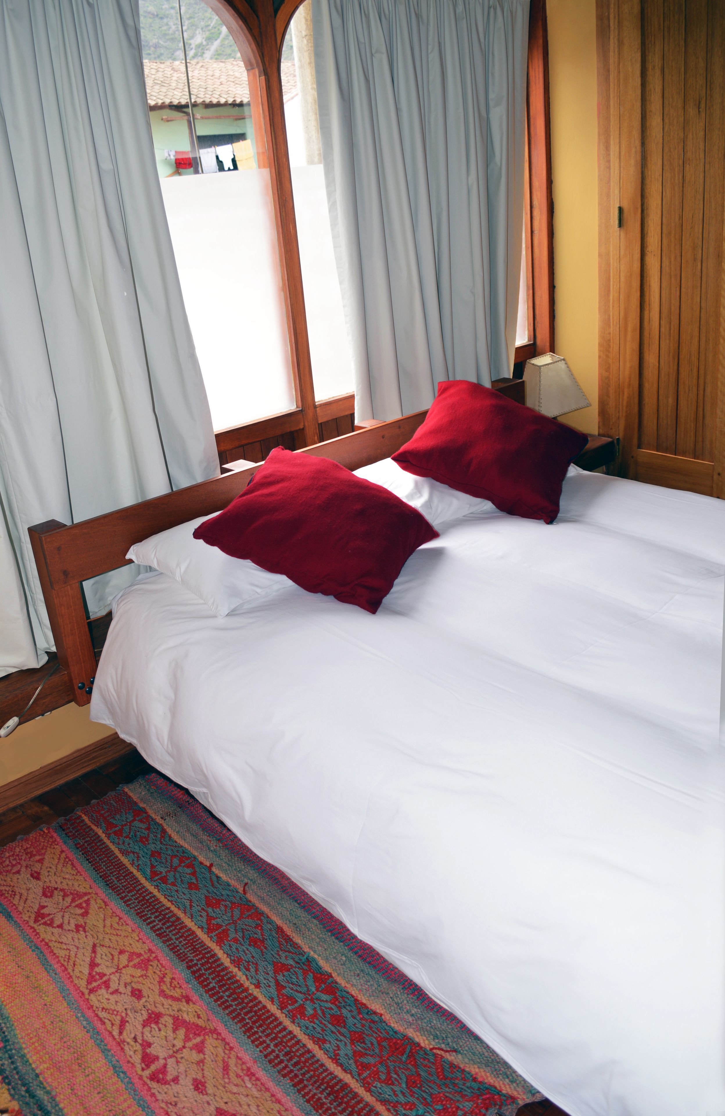 A bed with white bedding and two red pillows, a wooden headboard, and a patterned rug.