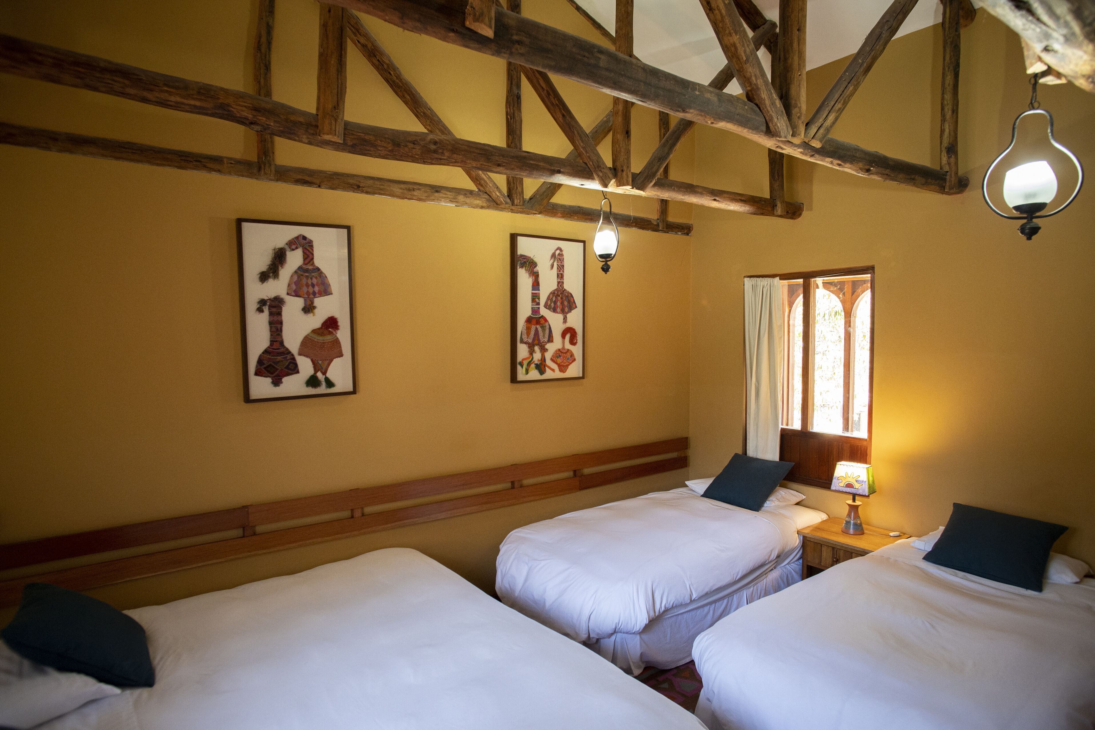 A hotel room with two single beds, wooden beams on the ceiling, and two framed pictures on the wall.