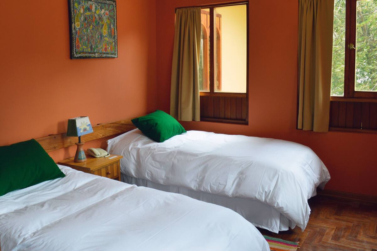 Une chambre avec deux lits, une tête de lit en bois, une table de chevet avec une lampe, un téléphone et un tableau coloré au mur.