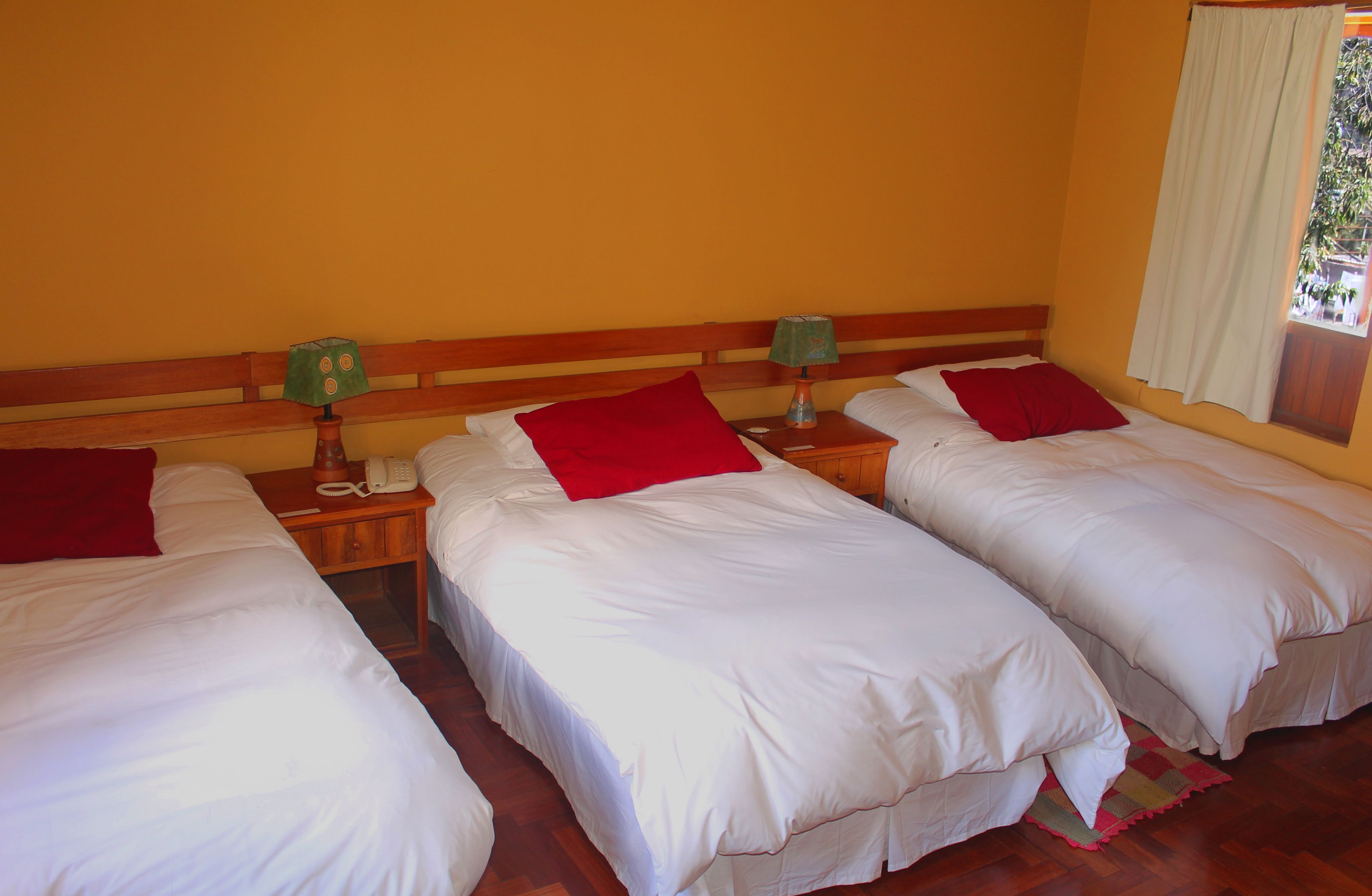 A room with three single beds, wooden headboards, and a nightstand with a lamp and phone.