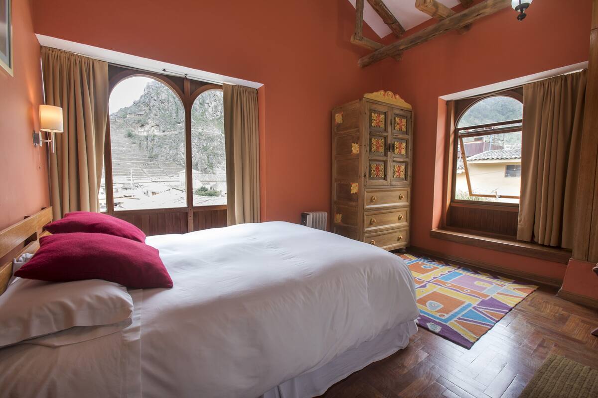 Une chambre à coucher avec un grand lit, une commode en bois et deux fenêtres avec des rideaux.