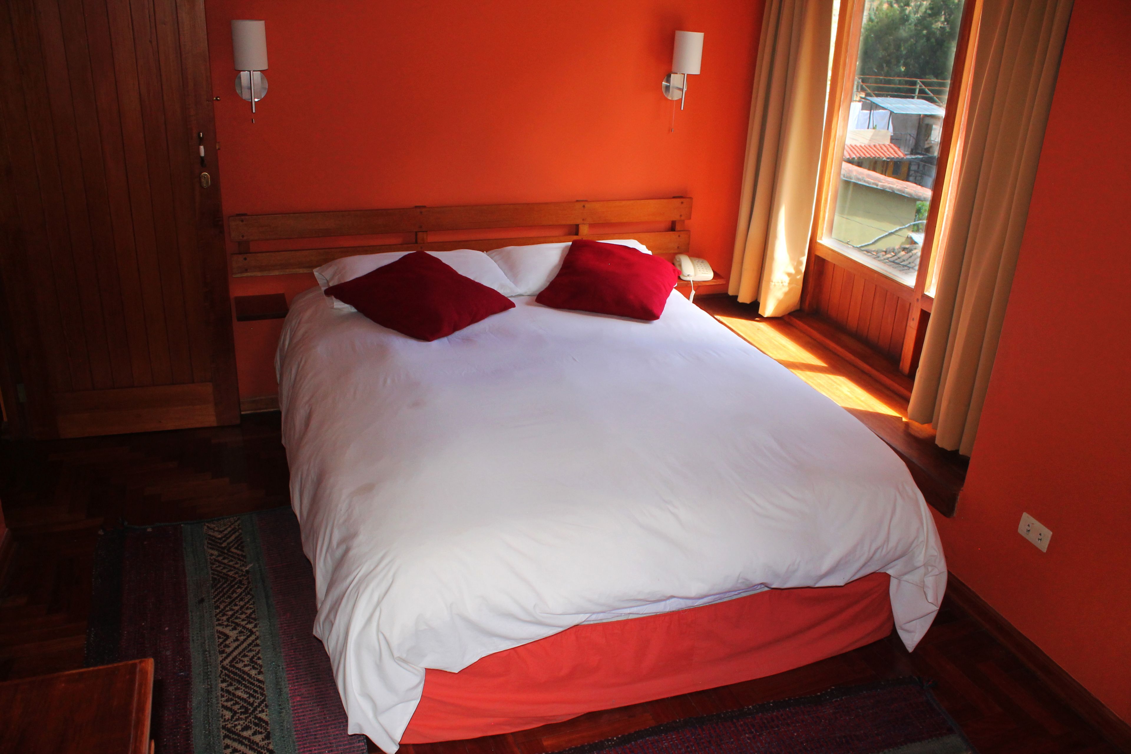 A bed with white and red bedding, wooden headboard, and two red pillows.