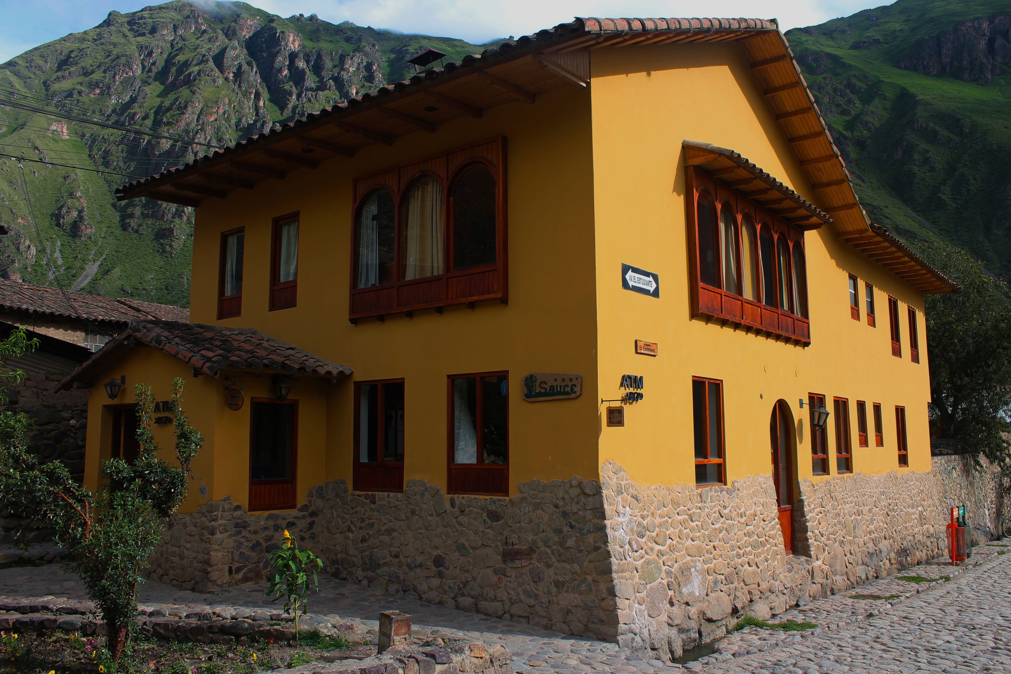 Un edificio amarillo con paredes de piedra y ventanas de madera, situado en una zona montañosa.