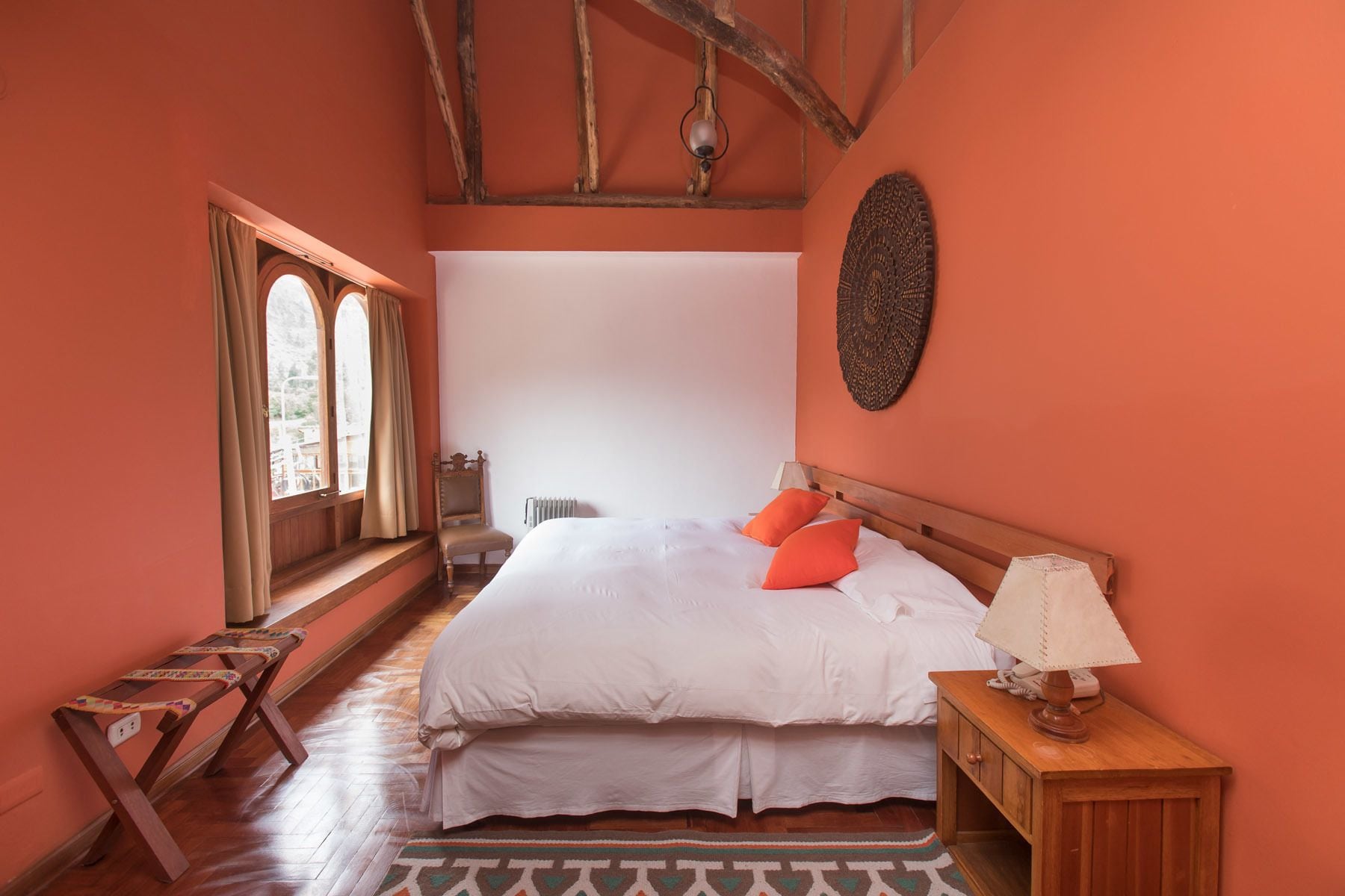 Un dormitorio con una cama grande, una mesita de noche de madera, una silla y un ventanal con cortinas.