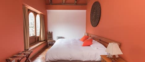 Un dormitorio con una cama grande, una mesita de noche de madera, una silla y un ventanal con cortinas.