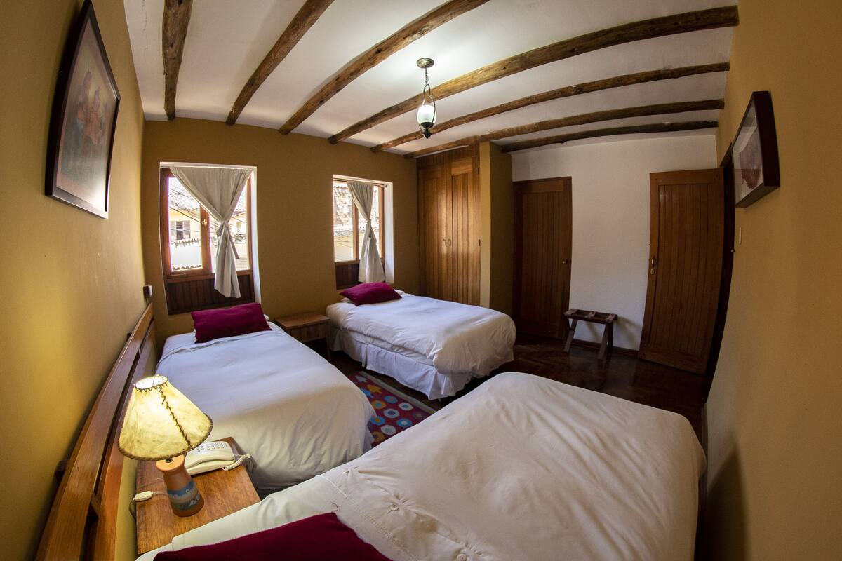 Une chambre avec deux lits, un plafond en bois et une petite table avec une lampe.