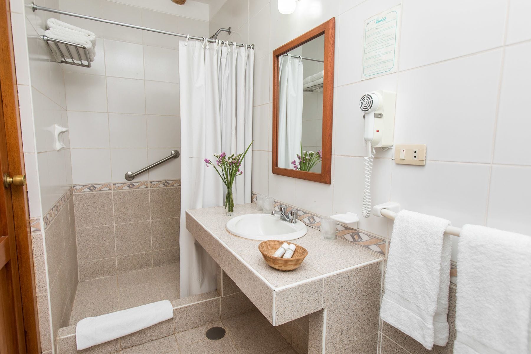 Une salle de bain équipée d’une douche, d’un lavabo, d’un miroir, d’un téléphone et d’un porte-serviettes.
