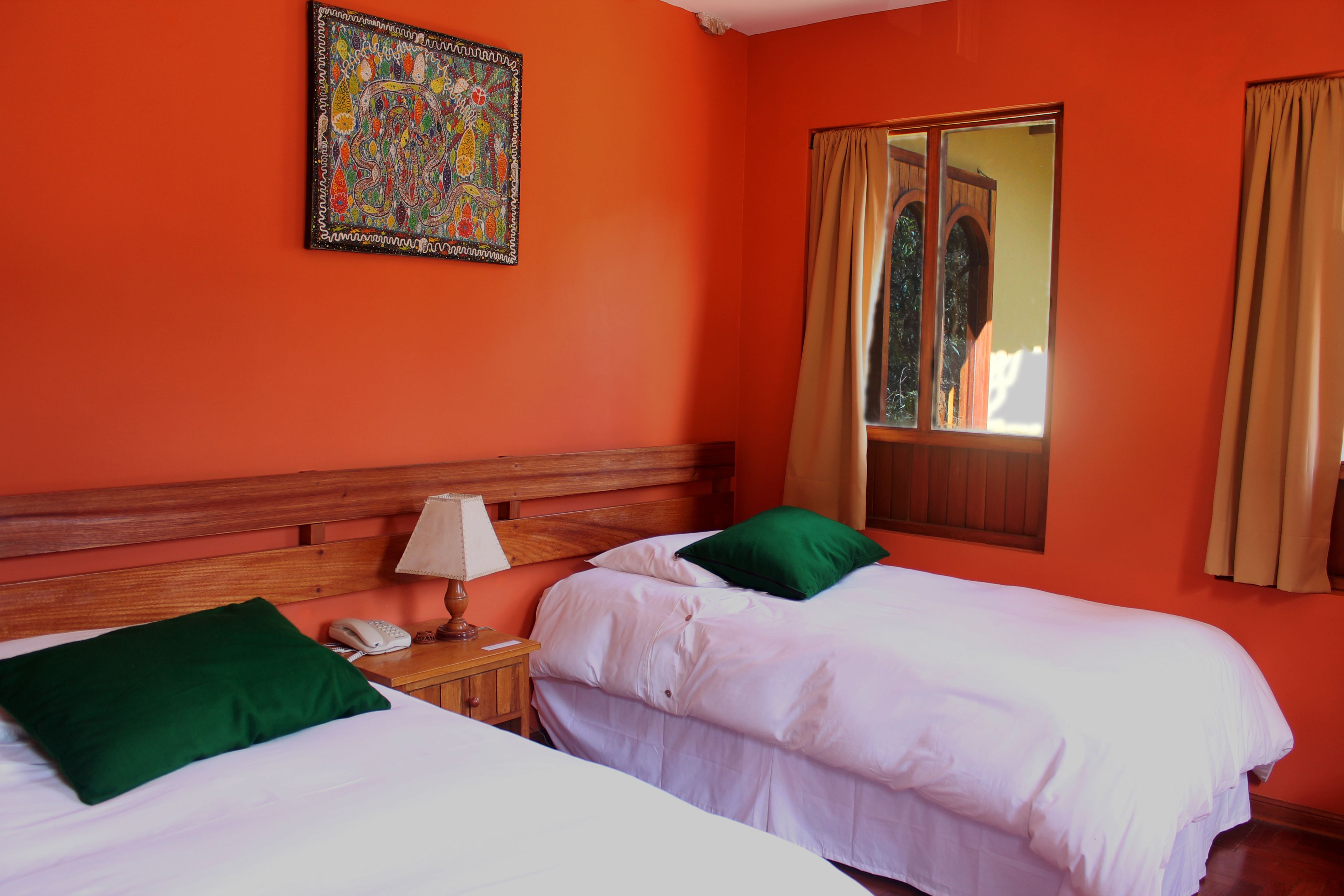 A room with two beds, a wooden headboard, a nightstand with a lamp, a telephone, and a colorful painting on the wall.