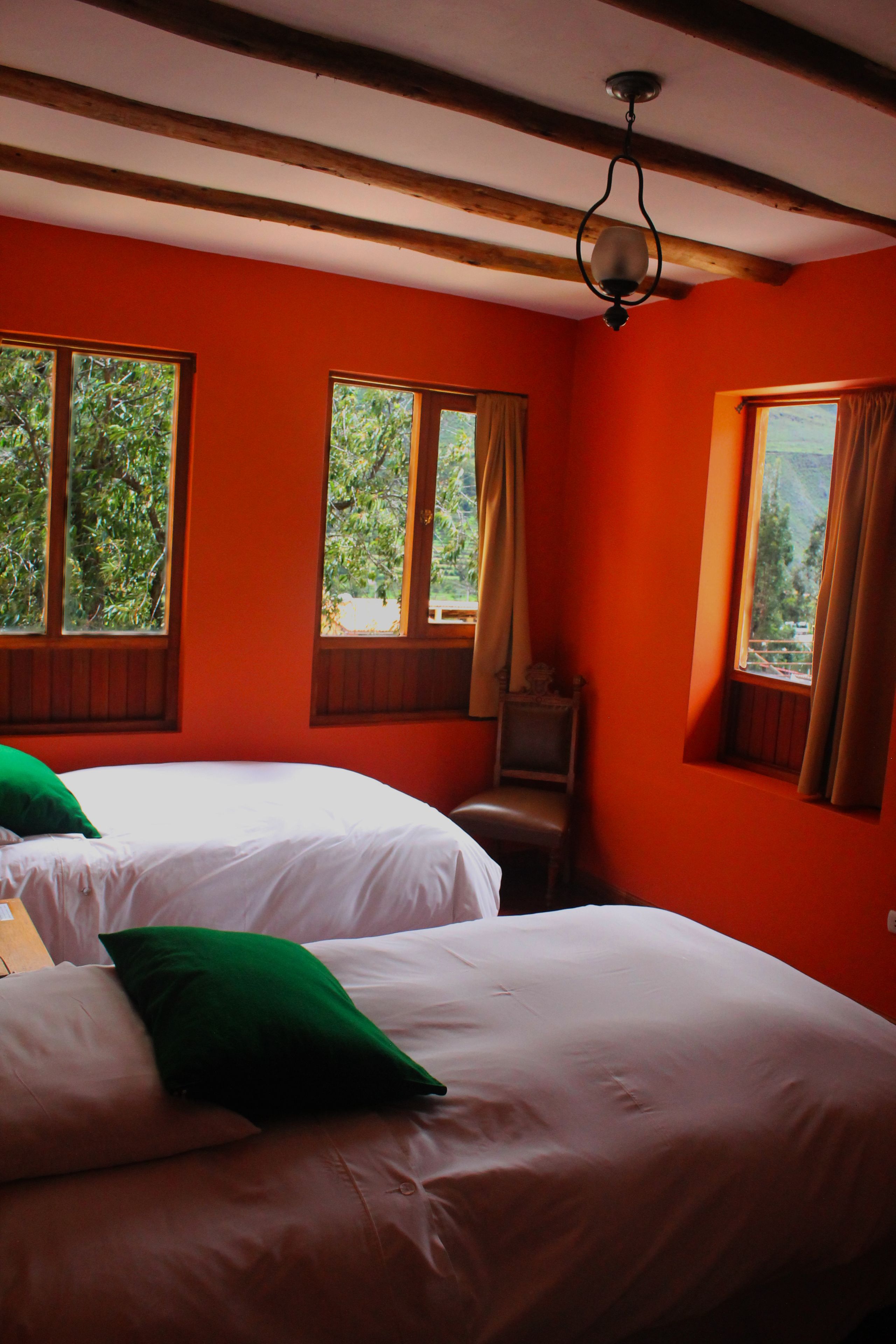 Une chambre avec deux lits, des poutres en bois au plafond et de grandes fenêtres avec des rideaux.