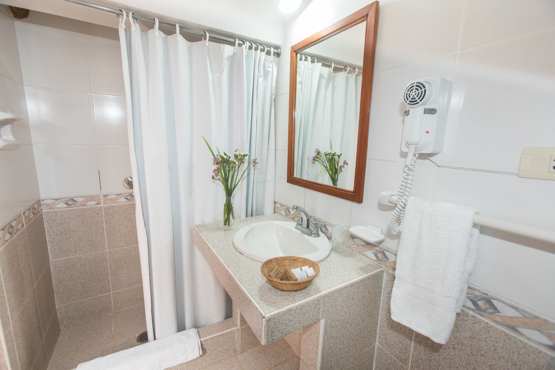 A bathroom with a shower, a sink, a mirror, a hairdryer, and a towel rack.