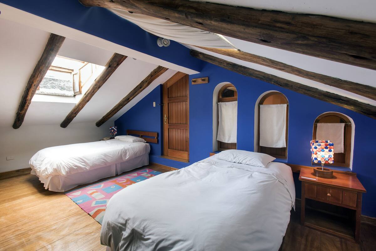 Une chambre avec deux lits, un plafond en bois, une lucarne et un tapis coloré.