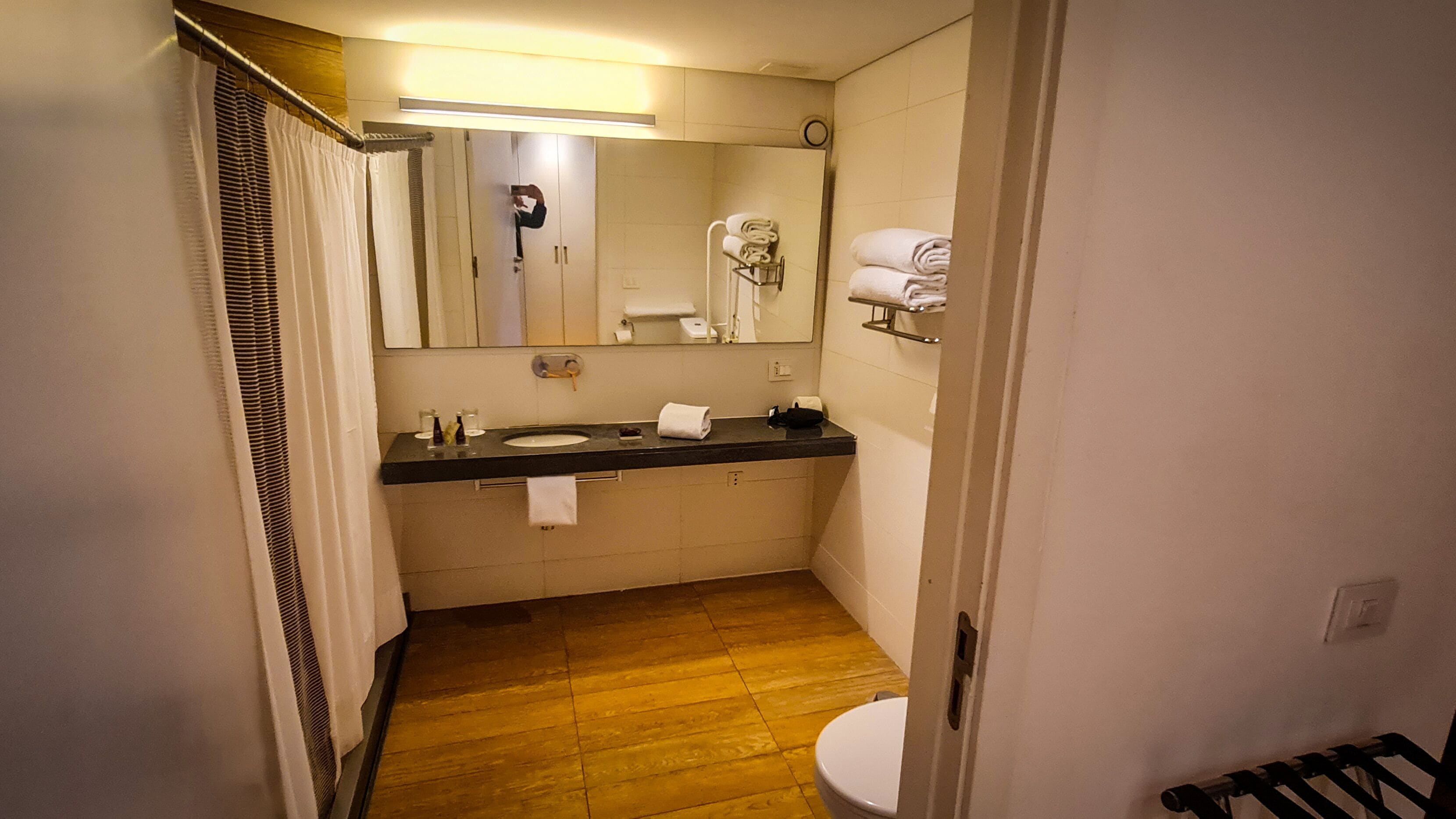 Un baño pequeño con suelo de madera, un lavabo, un espejo y un perchero para toallas.