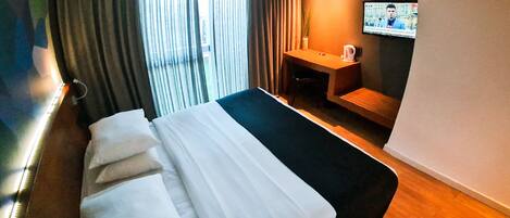 A hotel room with a bed, a TV on the wall, a small table, and a window with curtains.