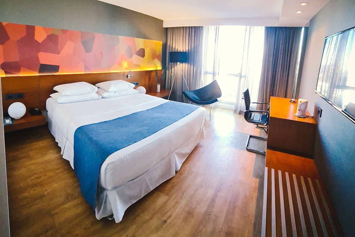 A modern hotel room with a large bed, a desk, and a chair.