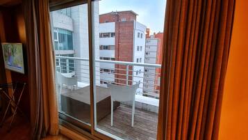 A balcony with white chairs, a small table, and a view of adjacent buildings.