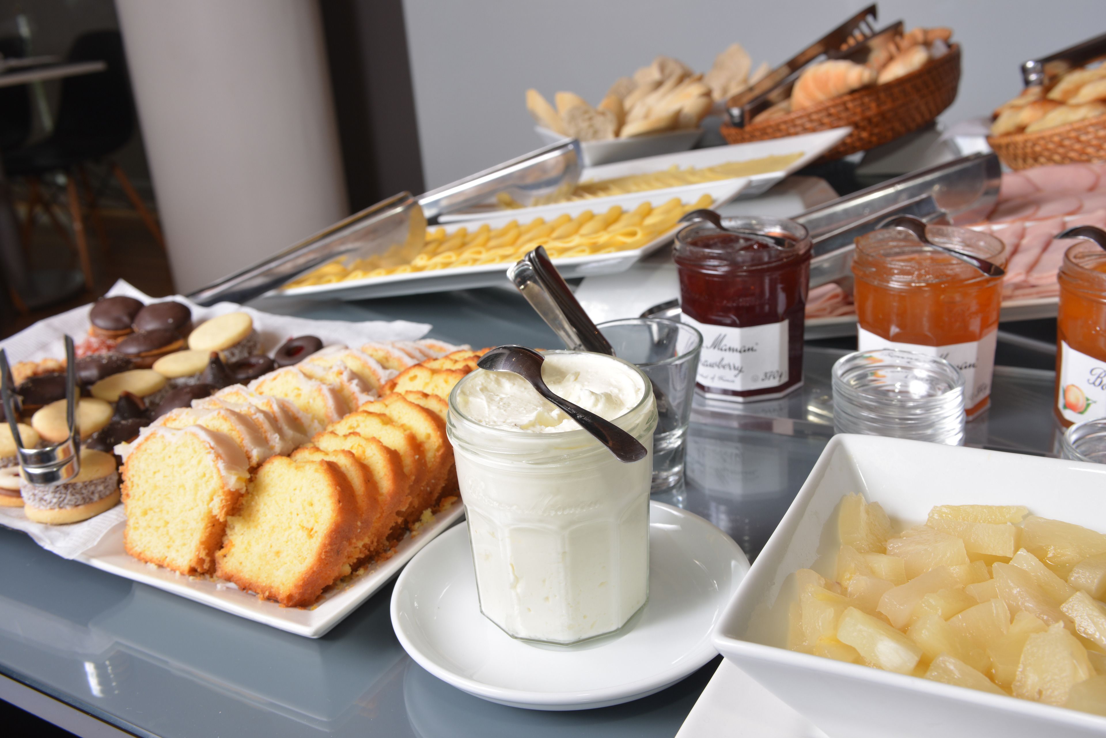 Une table de buffet proposant divers plats, notamment des pâtisseries, un pot de crème et un saladier rempli de morceaux d’ananas.