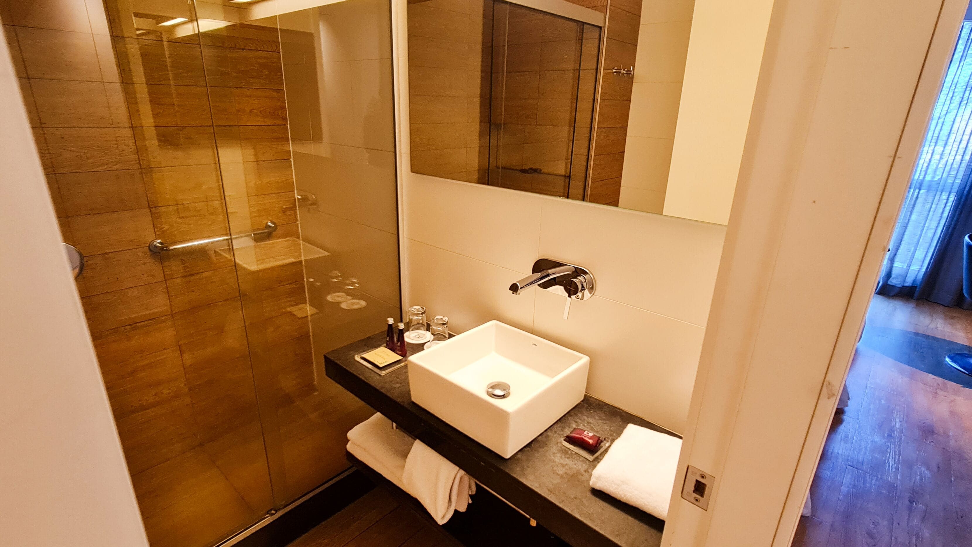 Un bany modern amb plat de dutxa de vidre, un lavabo blanc i un mirall gran.