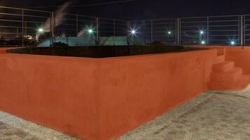 Un espacio exterior rectangular con piso de baldosas, rodeado por un muro bajo y una cerca metálica.