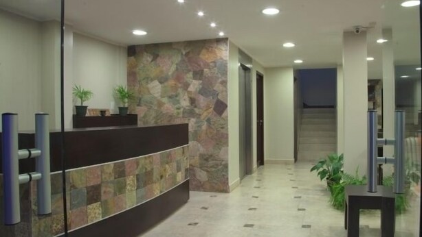 A reception area with a stone wall, a reception desk, and a staircase leading to another floor. - Munay Ledesma (Libertador General San Martin)