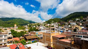 Un área urbana densamente poblada con una mezcla de edificios residenciales y comerciales, una destacada torre del reloj y un telón de fondo montañoso.