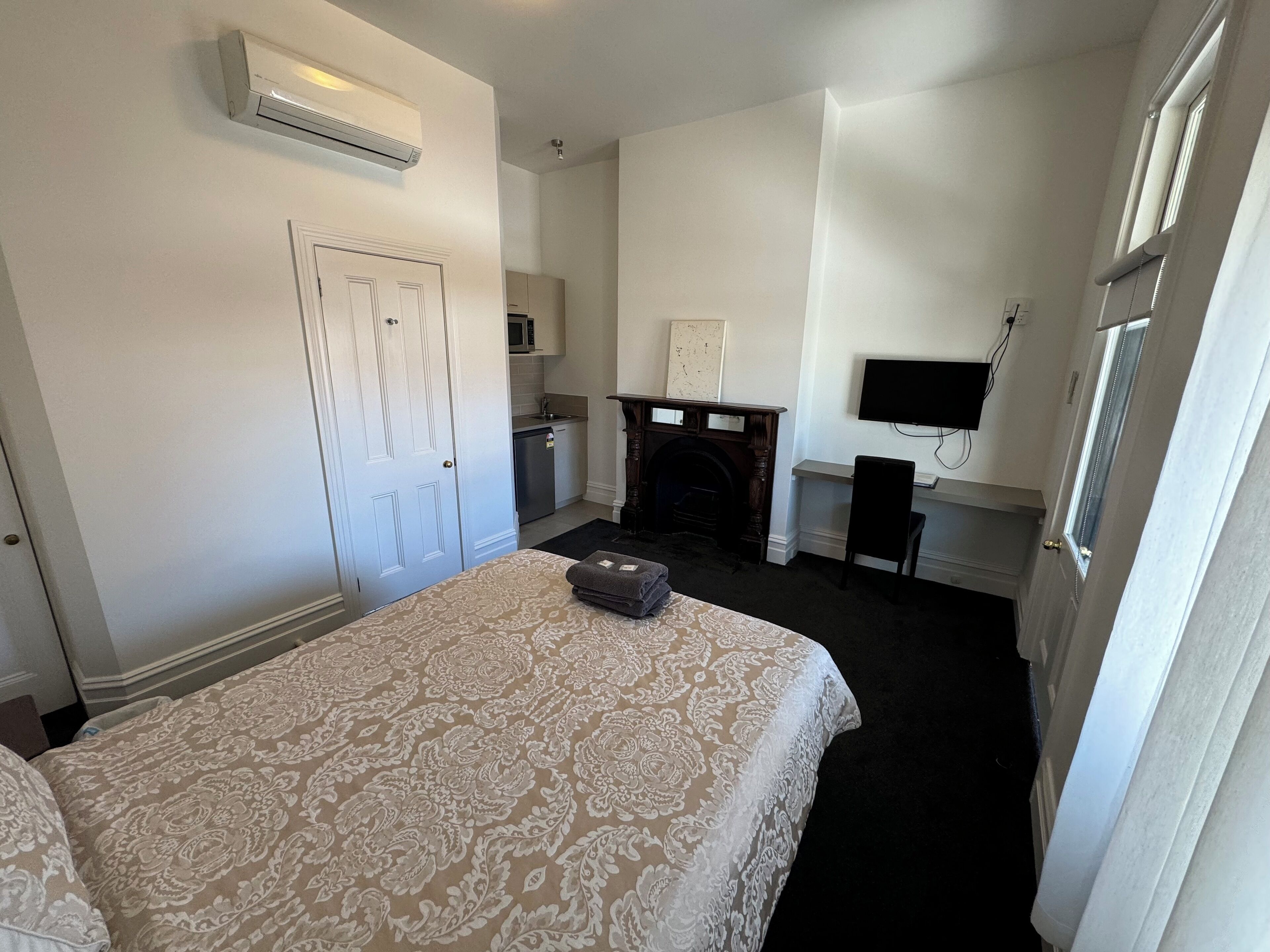 A hotel room with a bed, a fireplace, a television, and a door.