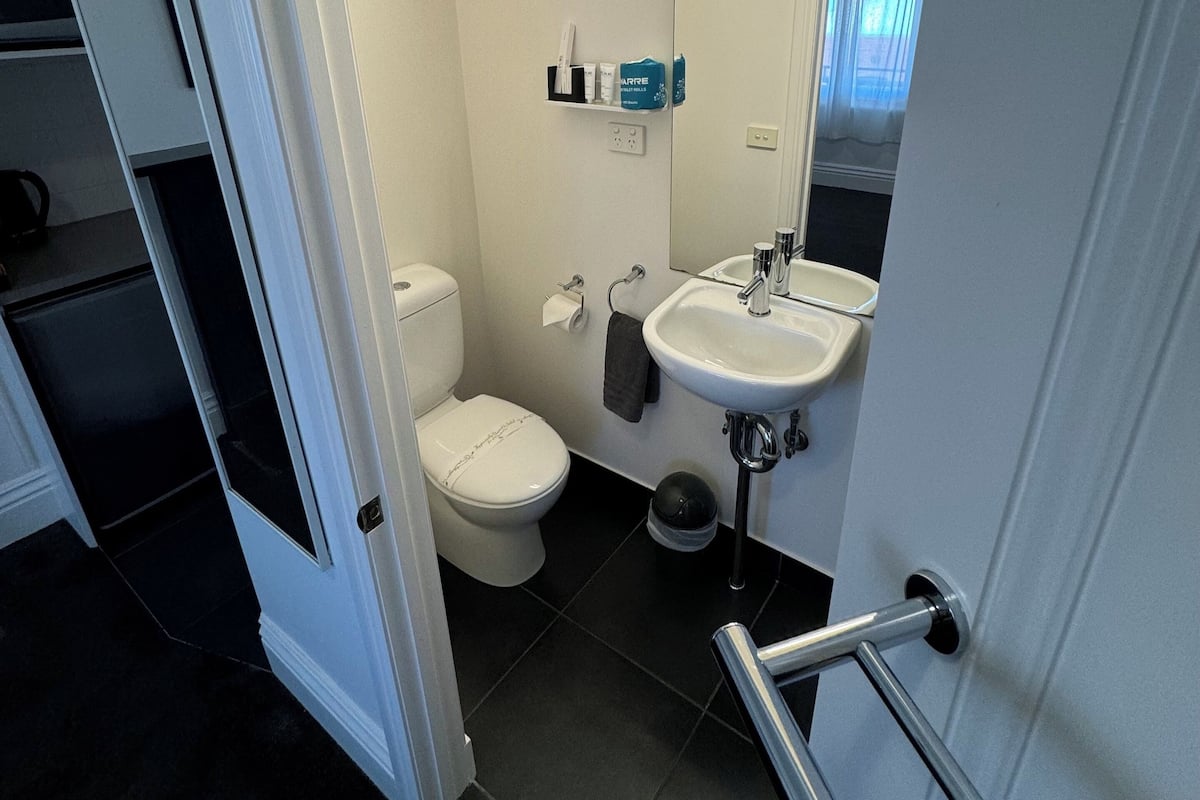 A compact bathroom with a toilet, sink, and mirror. A towel hangs on the wall, and a small shelf holds toiletries.