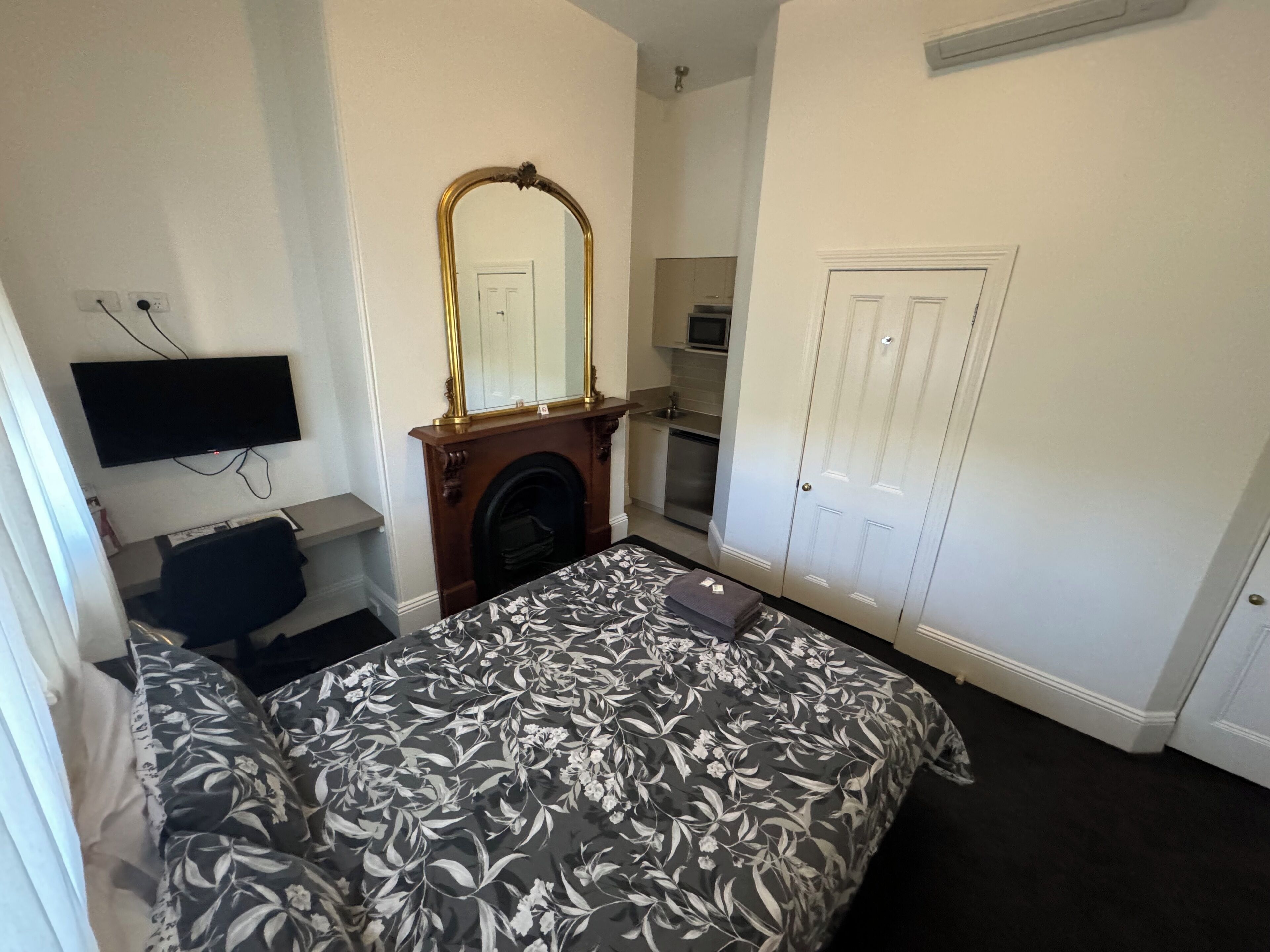 Un dormitorio con cama, chimenea, televisión montada en la pared, armario y puerta.