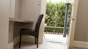 Ein Zimmer mit einem schwarzen Sessel, einer weißen Tür und Blick auf einen Garten mit Bäumen und einer Hecke.