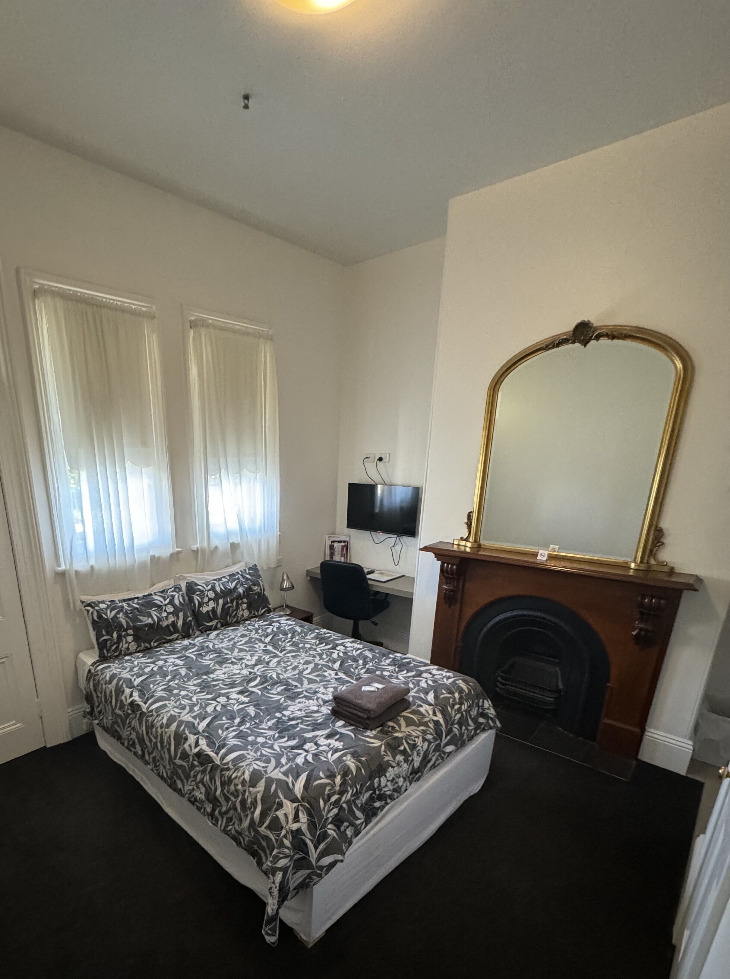 A bedroom with a bed, a desk, a television, and a fireplace.