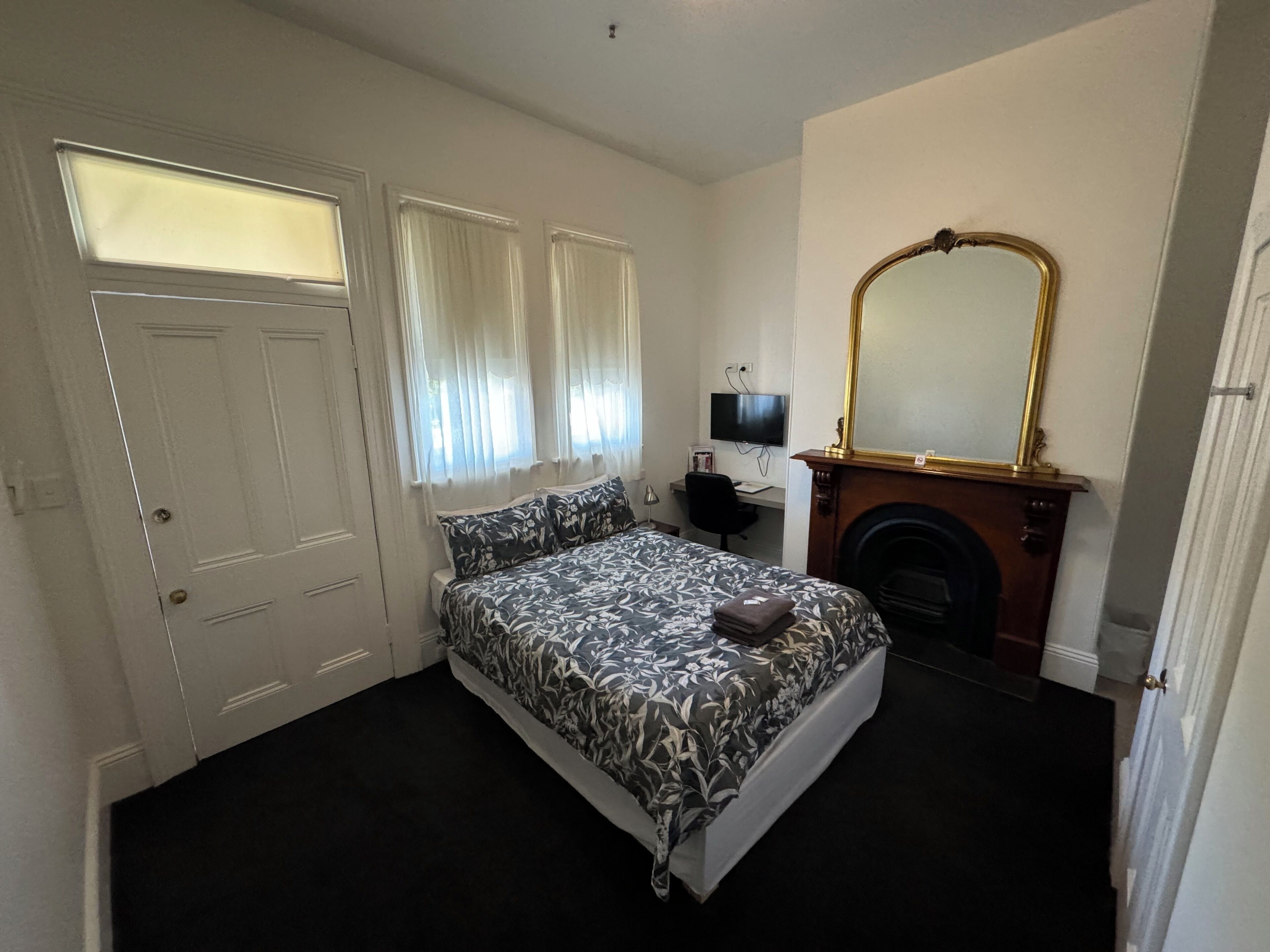 A bedroom with a bed, a desk, a television, a fireplace, and a mirror.
