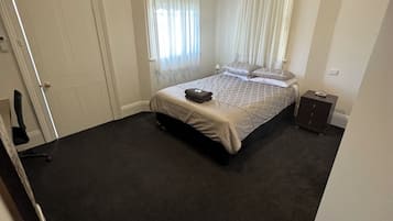 A bedroom with a bed, a nightstand, a desk, and a chair.