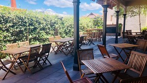 Eine Außenpatio mit Holztischen und -stühlen, einer Pergola und Blick auf Grünflächen und Gebäude im Hintergrund.