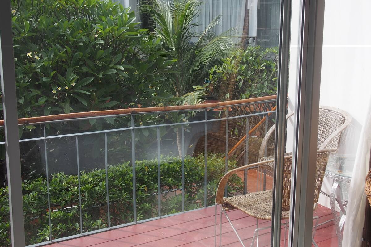 Un balcon doté d'une rambarde en métal, de chaises en osier et d'une végétation luxuriante.