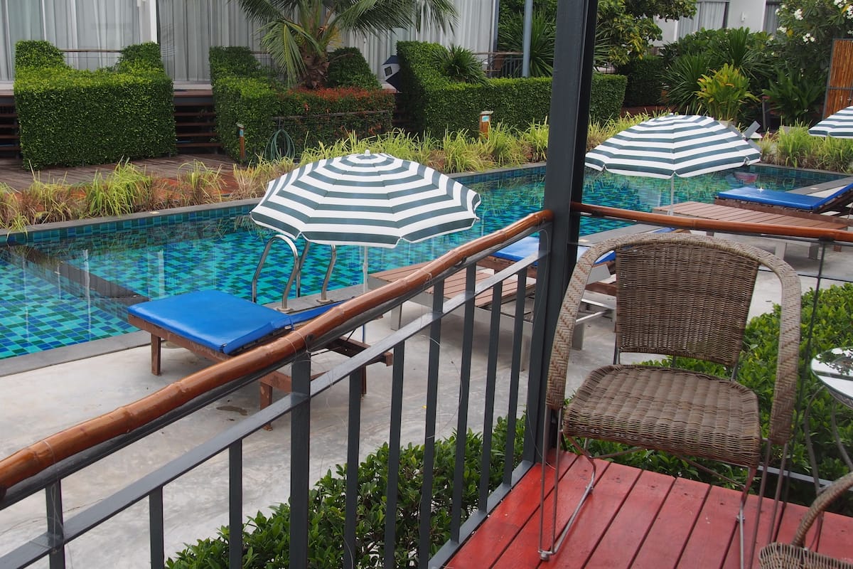 Un espace piscine agrémenté de chaises longues et de parasols, entouré de verdure et doté d’une terrasse en bois.