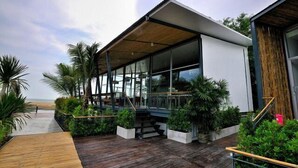A modern building with large glass windows, a wooden deck, and surrounding greenery. - LG Lemon Grass (Sattahip)