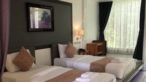 A hotel room with two beds, a bedside table, a lamp, a framed picture on the wall, and a window with curtains. - LG Lemon Grass (Sattahip)