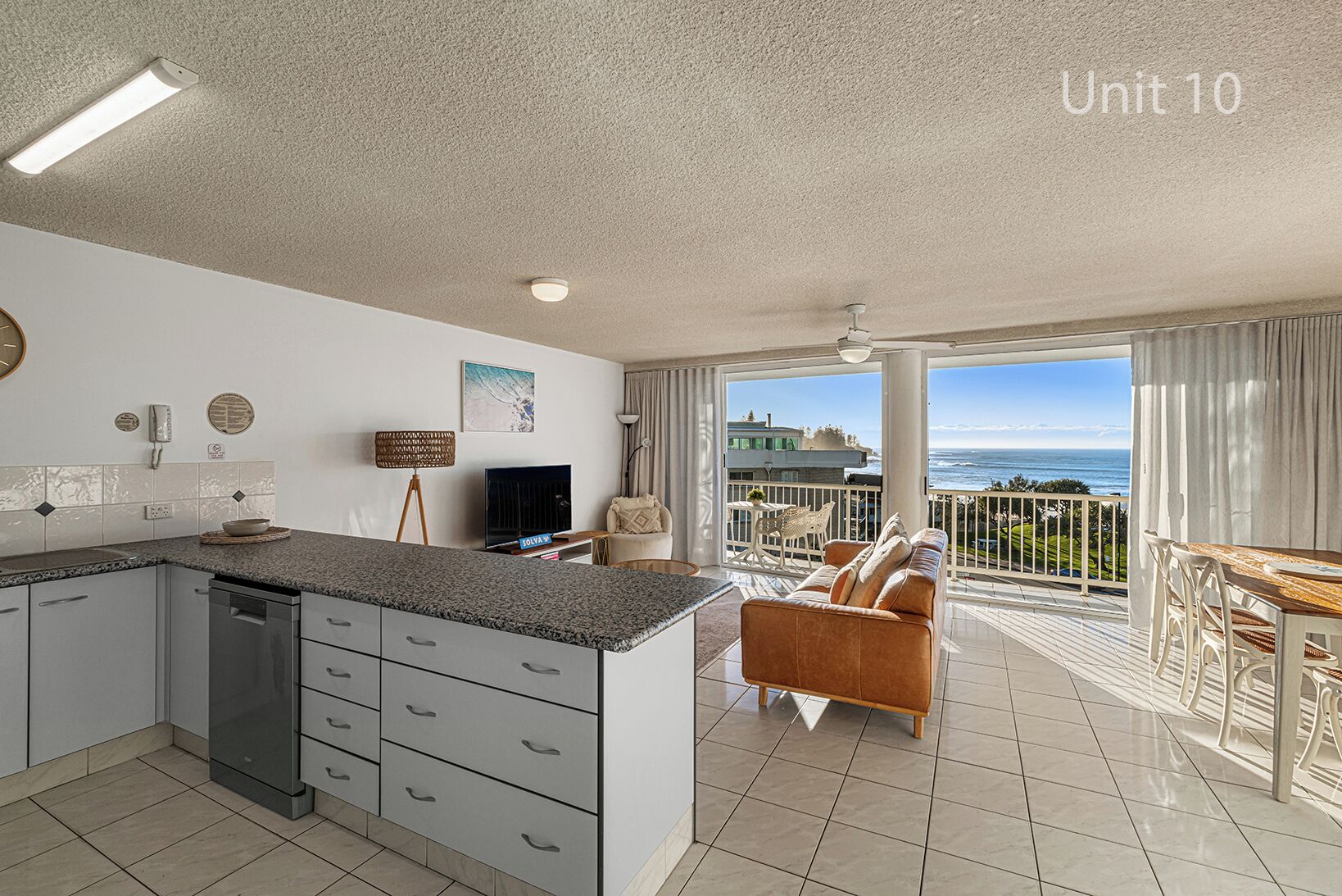 A modern kitchen with a built-in dishwasher, a dining area with a view of the ocean, and a balcony with a white railing.