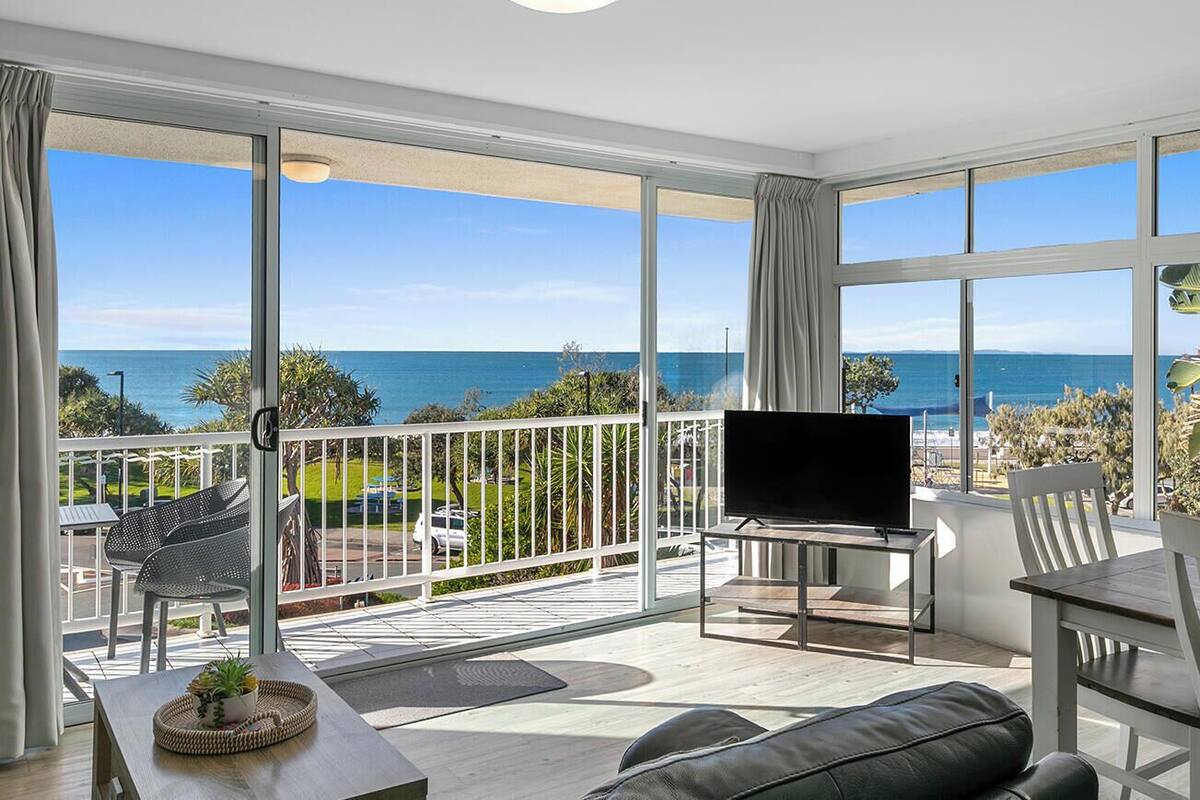 A balcony with a TV, seating, and a view of the sea.