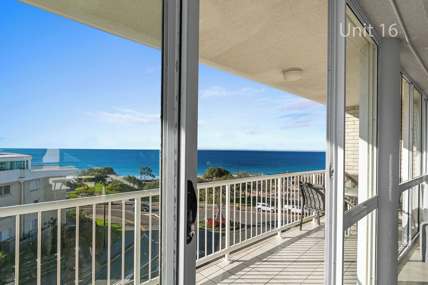 A balcony with a view of the ocean, a tiled floor, and a white railing.
