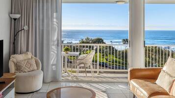 Een moderne woonkamer met een grote schuifglazen deur die uitkomt op een balkon met uitzicht op de oceaan.