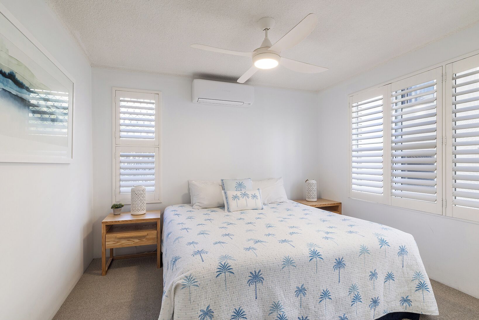 A bedroom with a bed, two nightstands, a ceiling fan, and a window with blinds.