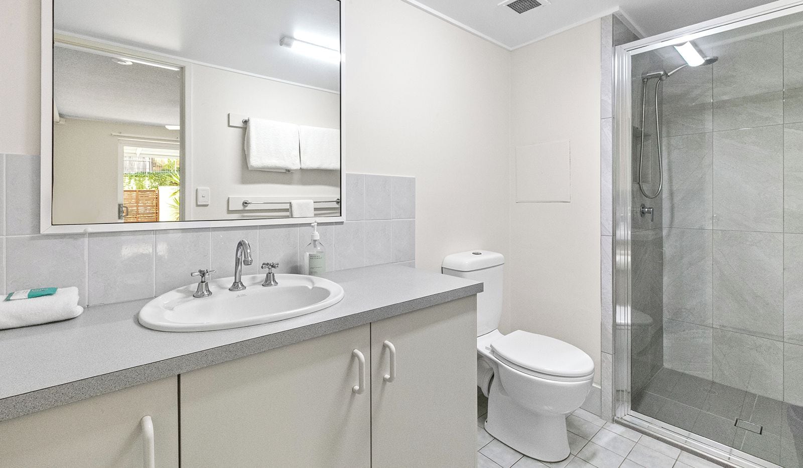Un baño moderno con lavamanos, espejo, inodoro y ducha.